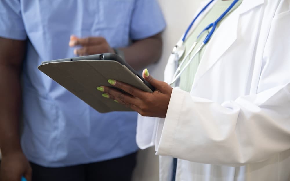 Profissional de saúde de jaleco branco segurando um tablet